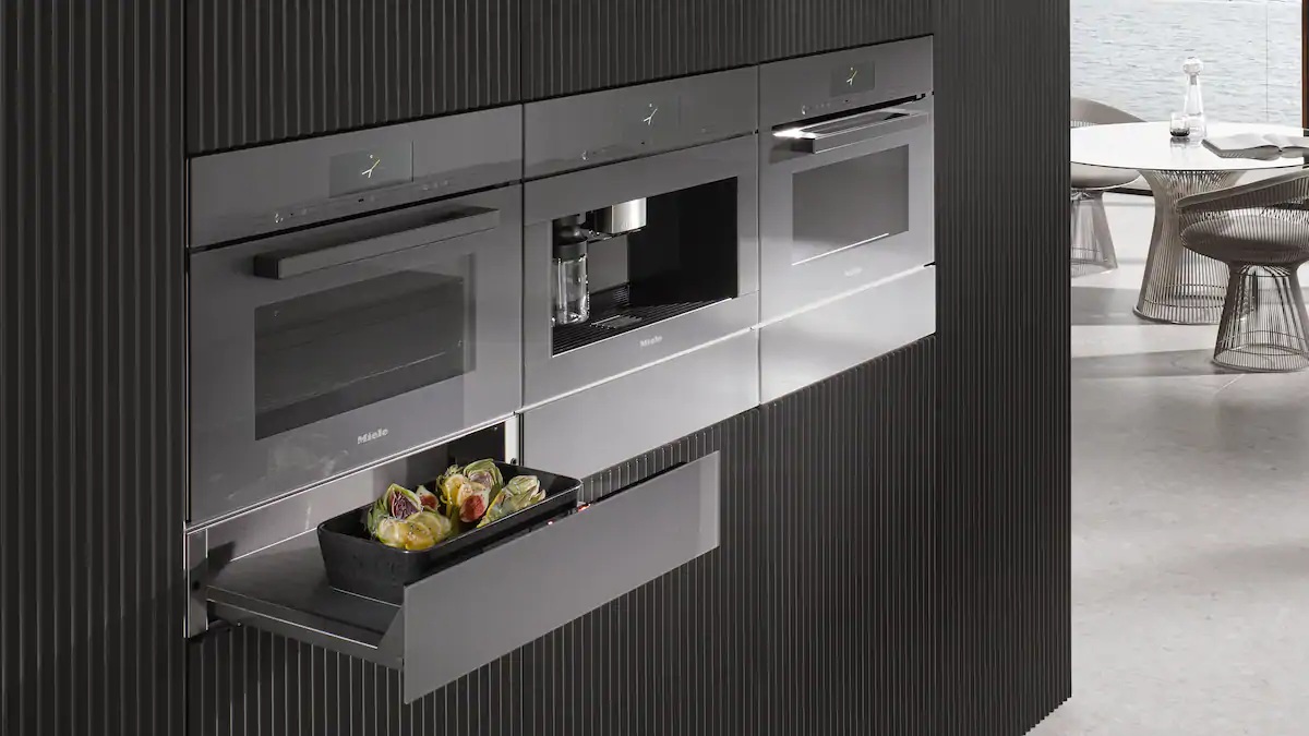Einbaugeräte in dunkler Küchenwand mit Backofen, Kaffeevollautomat und Wärmeschublade